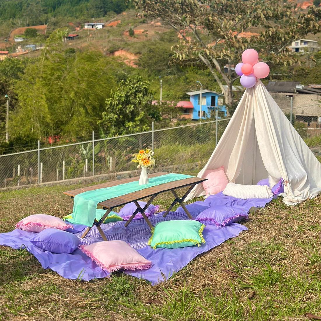Picnic al aire libre con teepee, cojines pastel y globos en la punta, sobre manta morada
