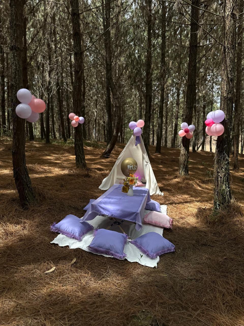 Picnic de cumpleaños en el bosque con racimos de globos colgados en los árboles y globo dorado 'Feliz'