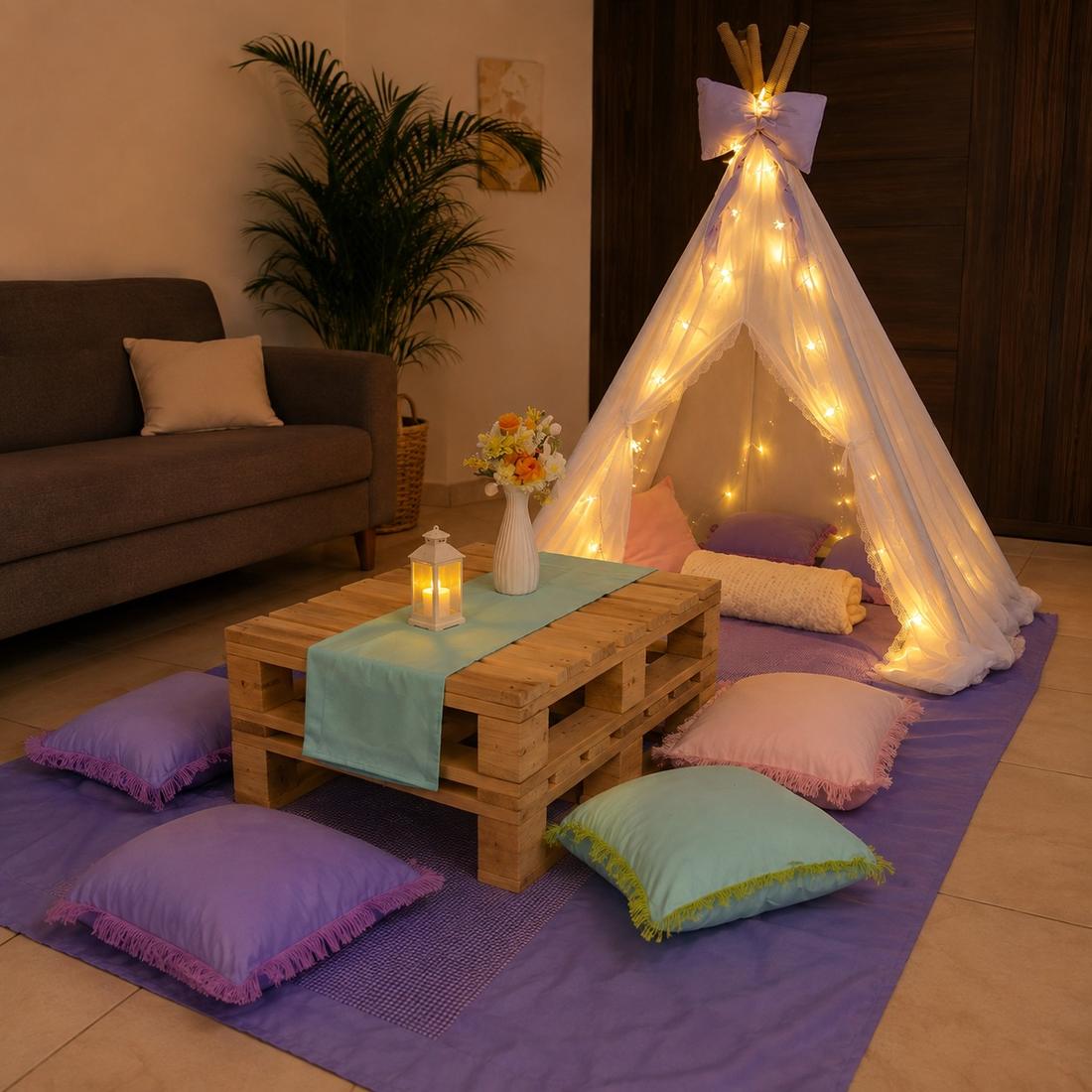 Teepee de pijamada iluminado con luces cálidas, cojines pastel y mesa de centro estilo estiba